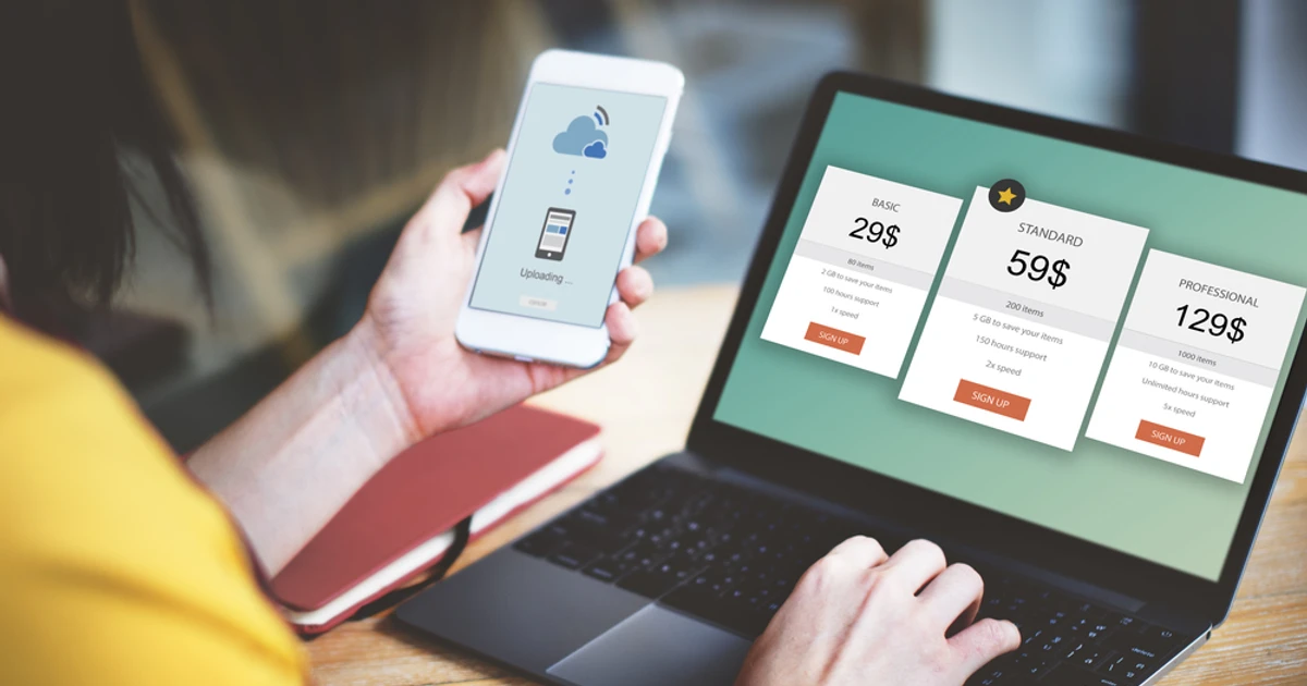 A person comparing SEO pricing plans and packages on a laptop screen while checking upload progress on a phone