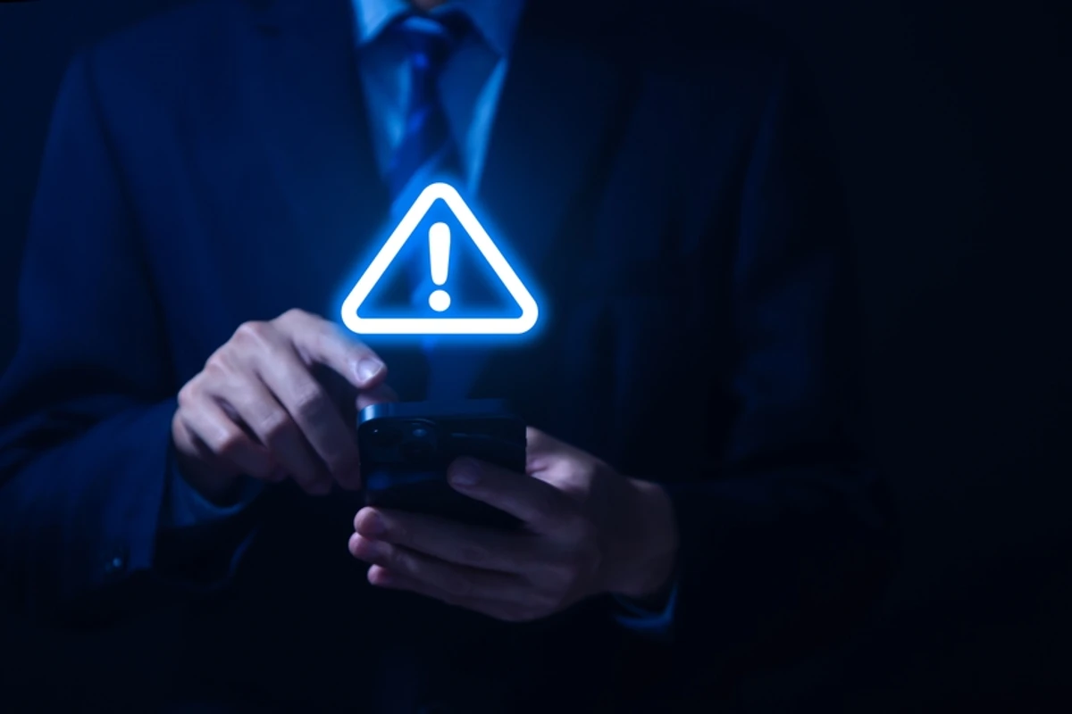 A glowing warning icon above a phone in a businessman's hands, representing red flags to watch for in SEO pricing and contracts